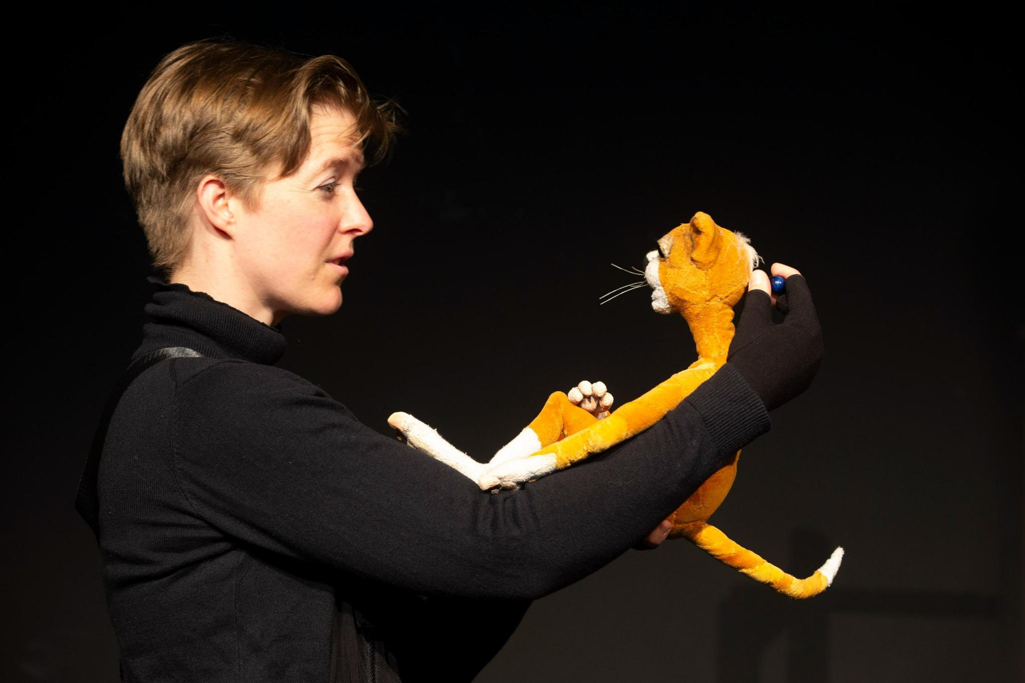 Lena Kießling in Bühnenlicht vor schwarzem Vorhang. Sie hält eine Katzenfigur, die mit ihr spricht.