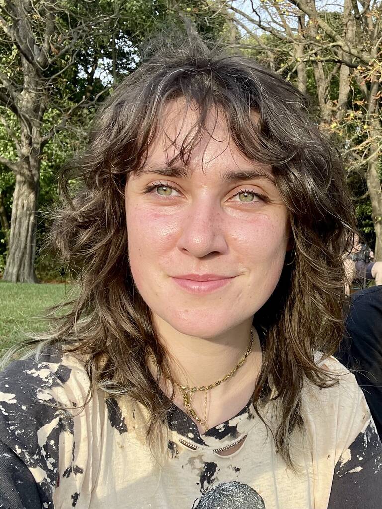 Portraitfoto von Nele Rennert. Im Hintergrund sind eine Rasenfläche und Bäume zu sehen.