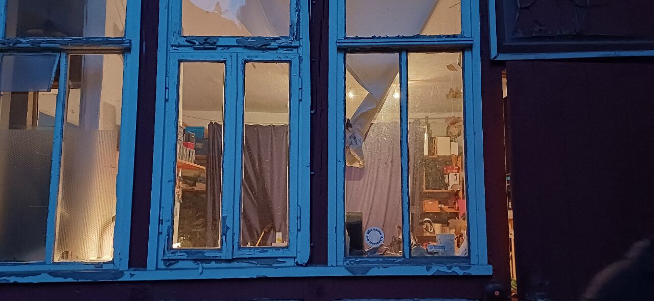 Blick durch blau-weiße Fensterrahmen von außen in die erleuchtete Werkstatt von Christoph Buchfink